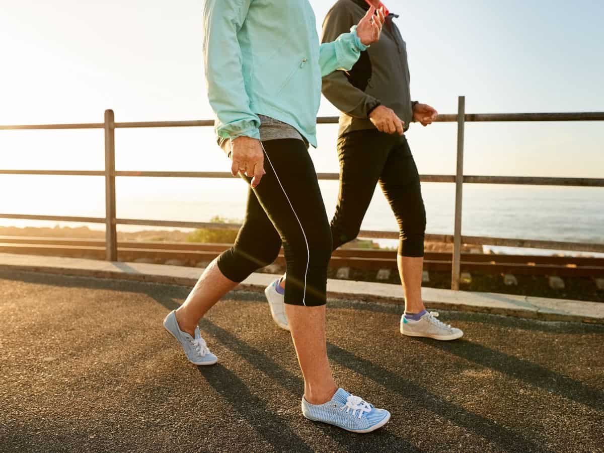 Two women walking on a boardwalk against a cloudy sky. Photo from neck down so you don't see faces.